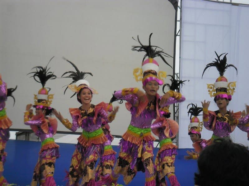 Dancers in pink and gold sequinned costumes and black feathered headdresses performing on stage